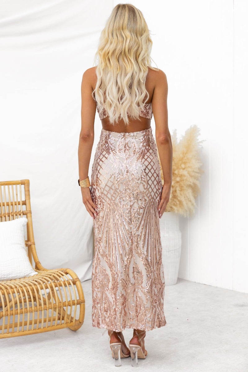 Back view of a luxurious sequin maxi dress with adjustable straps and a cut-out waist, model wearing light blonde hair.