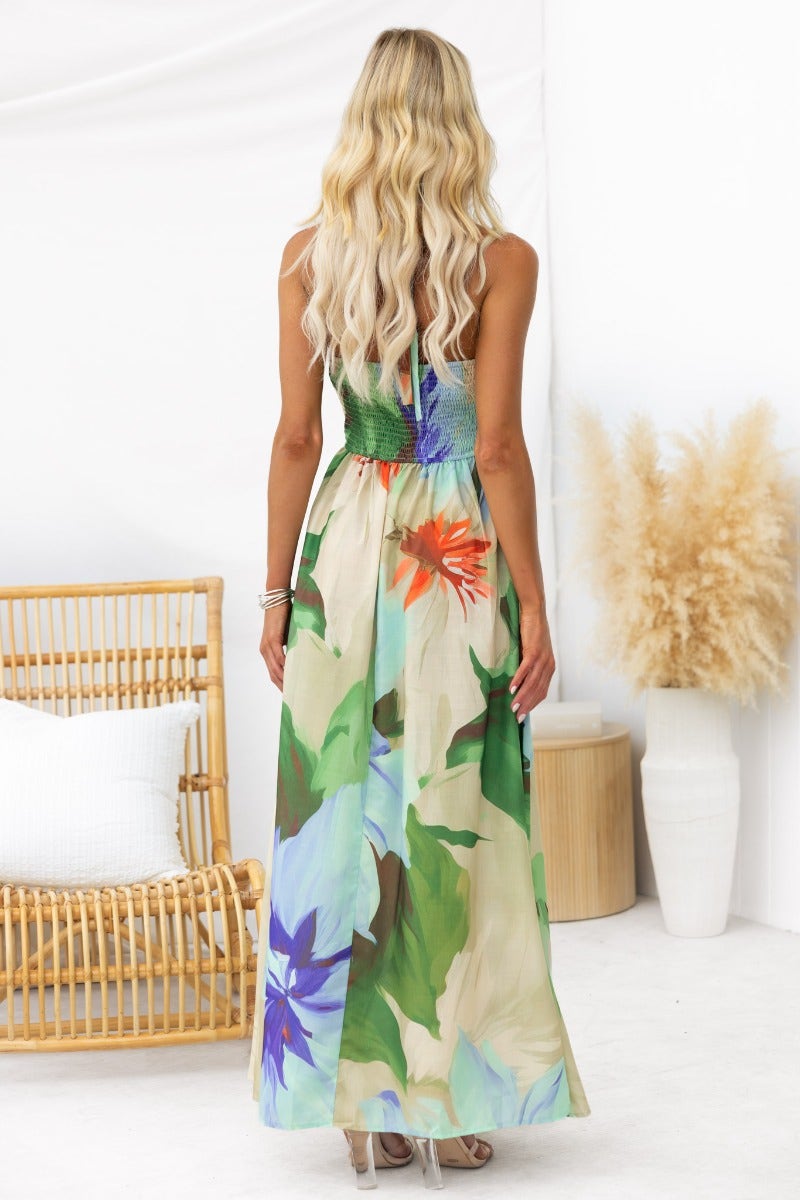 Back view of a woman in a floral print maxi dress with adjustable tie neckline, showcasing vibrant colors and light material.