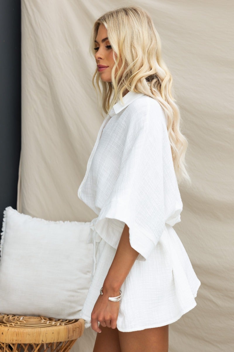 Model wearing the Rowson Playsuit in white, featuring a button-up collar and oversized fit, styled with a casual background.
