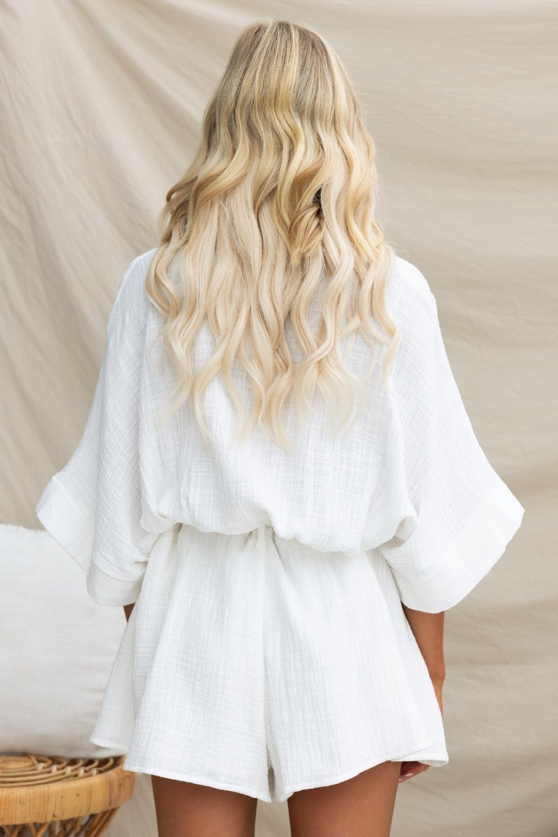 Back view of a woman in a white Rowson playsuit with flowing sleeves and wavy blonde hair.