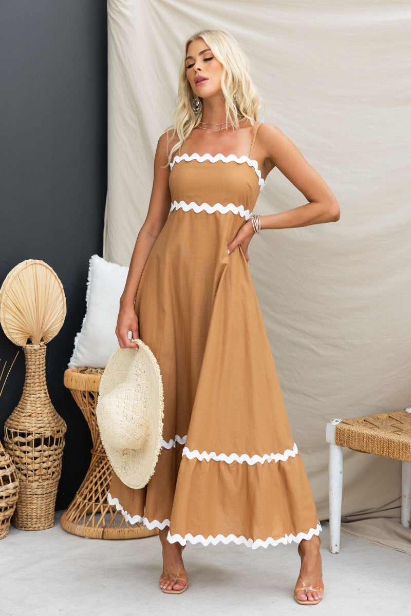 Model wearing Guyara Maxi Dress in tan with white trim, featuring adjustable straps and a flared skirt.