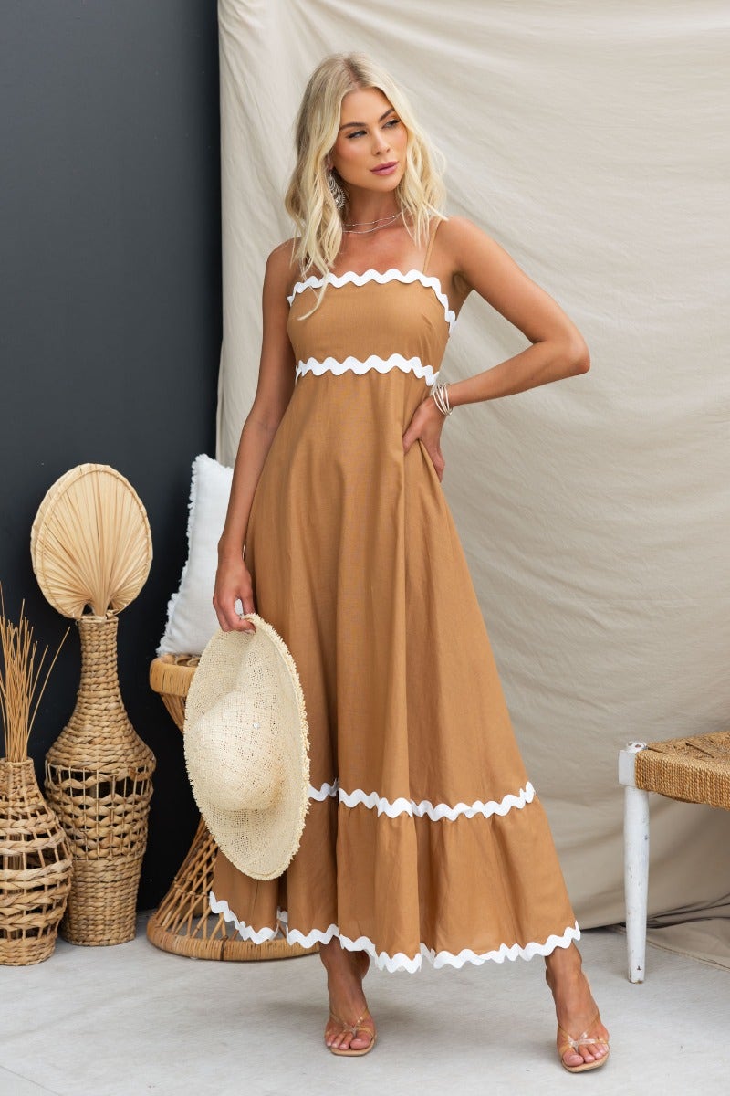 Guyara maxi dress in brown with white trim, featuring adjustable straps and a flowing silhouette, styled with a straw hat.