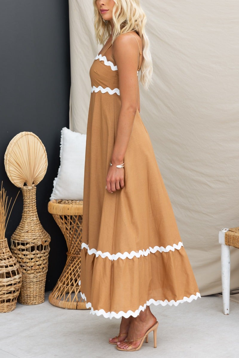 Side view of a woman wearing a Guyara Maxi Dress in brown with white scalloped trim, styled in a relaxed setting.