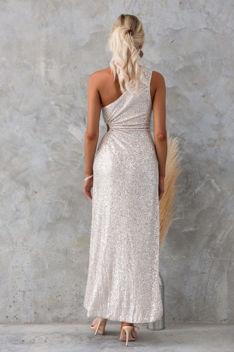 Back view of a woman in a sequin Tayan Maxi Dress with one-shoulder neckline and asymmetrical hemline.