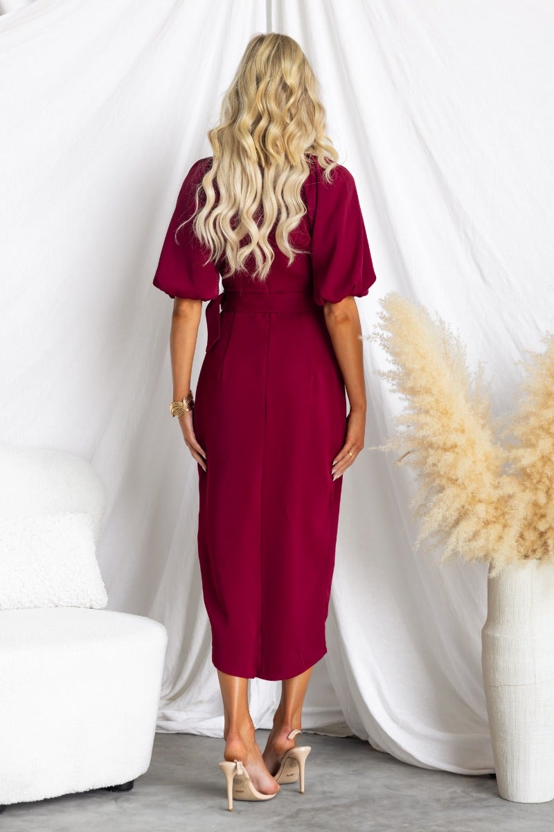 Rear view of a model wearing a burgundy Broadway Midi Dress with elastic sleeves and an asymmetric hemline.