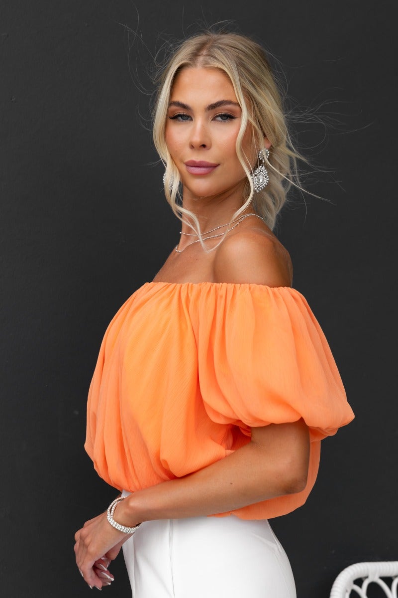 Model wearing the Adanna Top in vibrant orange, featuring an off-shoulder design and chiffon material.