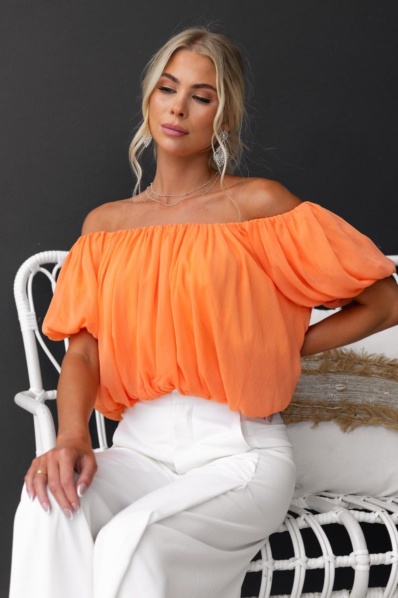 Model wearing the Adanna Top in vibrant orange, featuring an off-shoulder design and chiffon material.