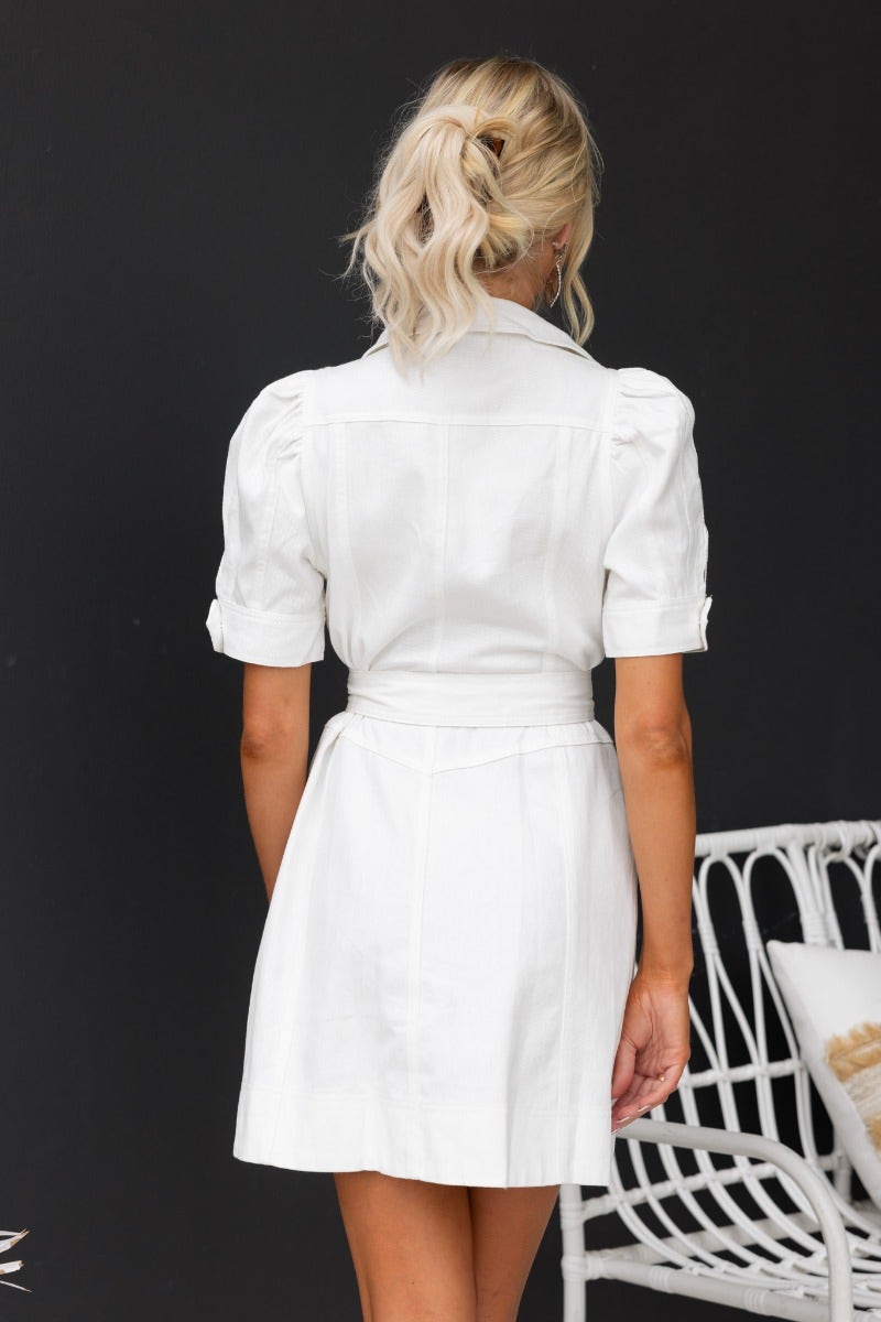 Model wearing a white denim dress with a collar and removable belt, showcasing a back view against a dark background.