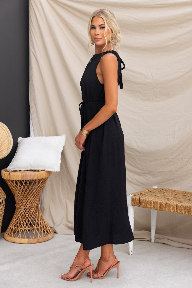 Model wearing the Iwaki Black Maxi Dress with adjustable neckline and pockets, styled with heels.
