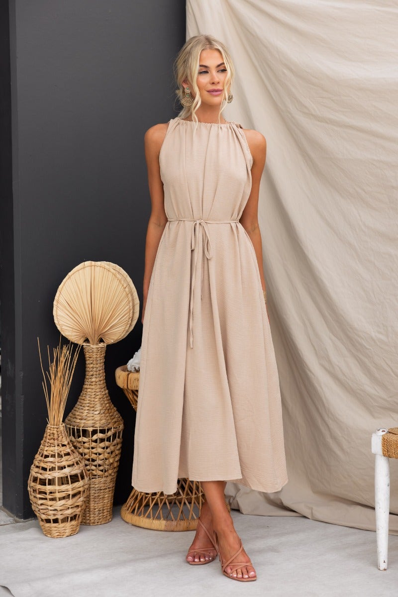 Model wearing Iwaki Maxi Dress in beige with adjustable neckline and pockets against a neutral backdrop.