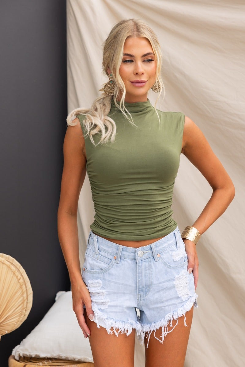 Model wearing olive green Beau Top, a cotton blend tank with a high neckline and ruched sides, paired with denim shorts.