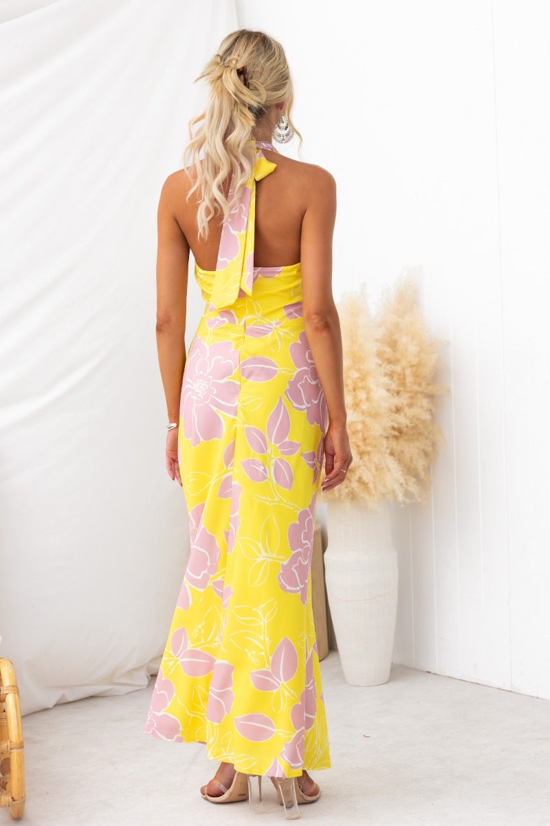 Back view of a woman in a floral print yellow maxi dress with adjustable tie halter neckline.