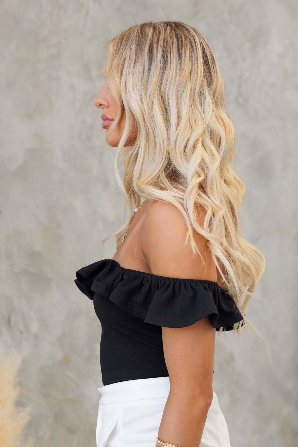 Side view of a woman wearing a black off-shoulder Bellar bodysuit with ruffle detailing.
