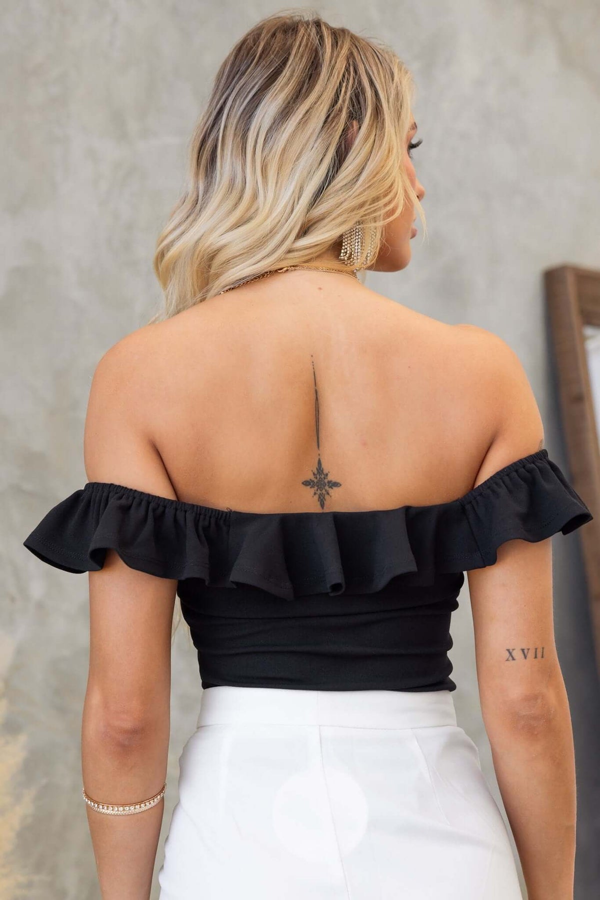 Back view of a woman wearing a black off-shoulder Bellar bodysuit with ruffle details.