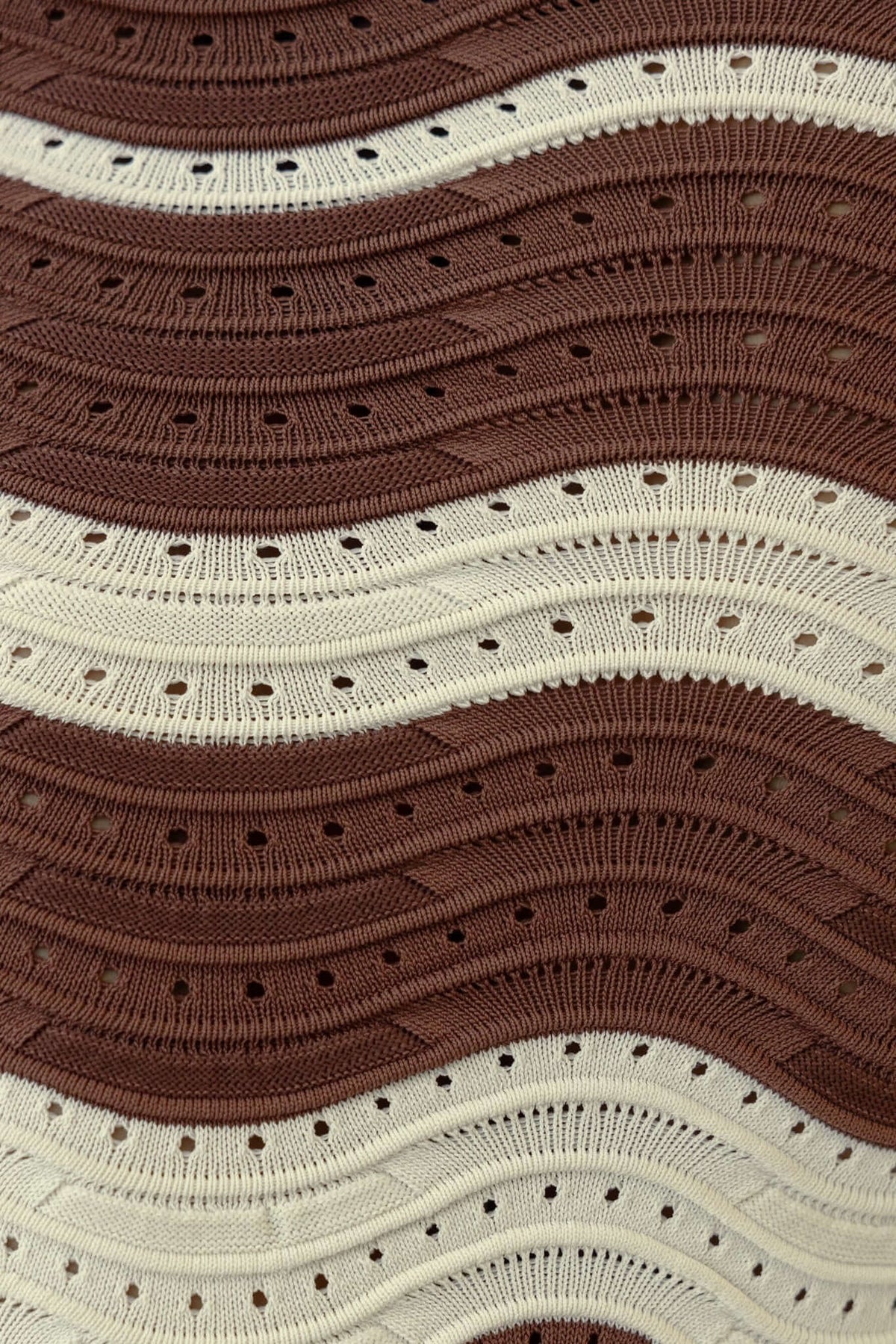 Close-up of a textured knit fabric featuring wavy stripes in brown and cream colors.