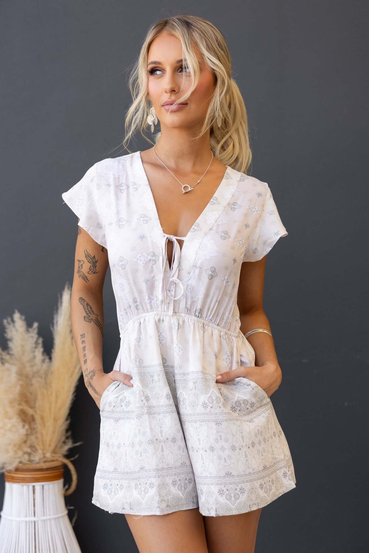 Kenny Playsuit in linen look with tie detail, elastic waistband, and pockets, modeled by a woman against a dark background.