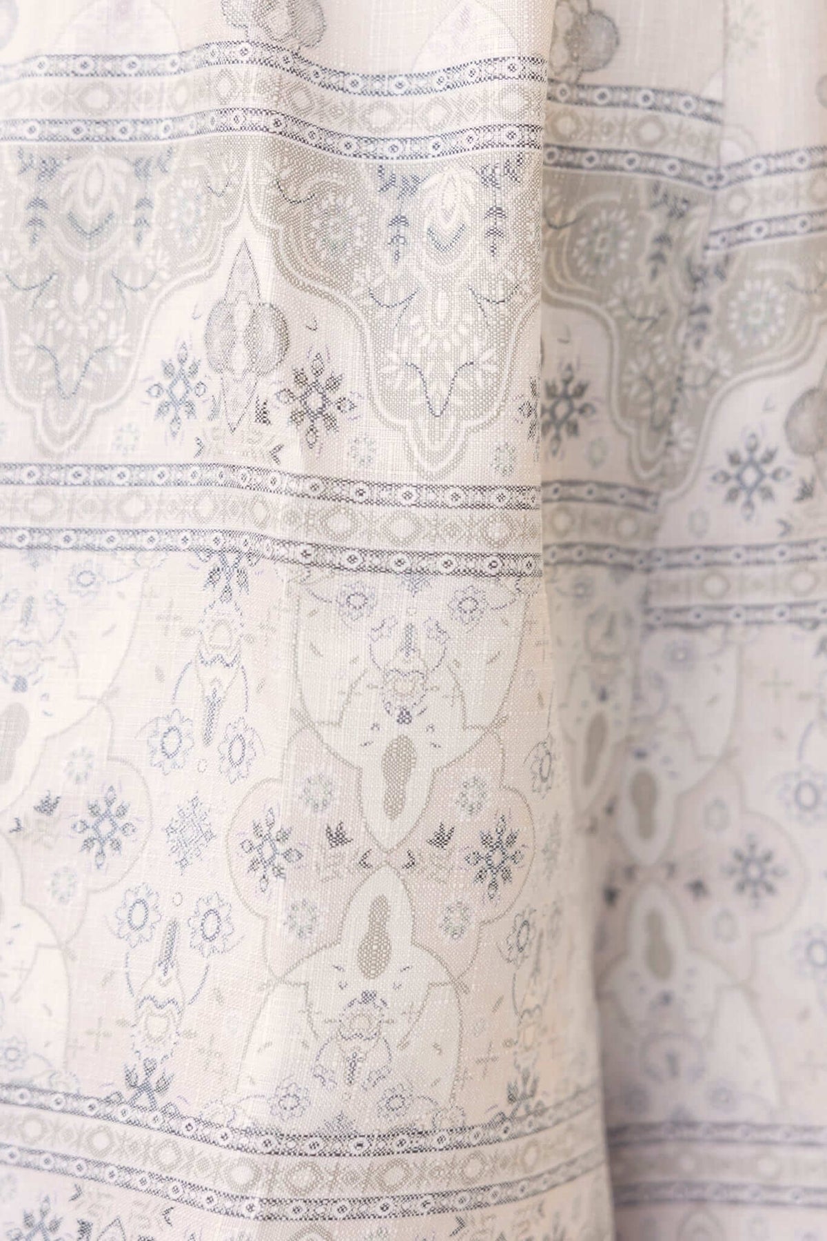 Close-up of intricate patterned fabric with grey and white designs, showcasing a delicate linen look and feel.