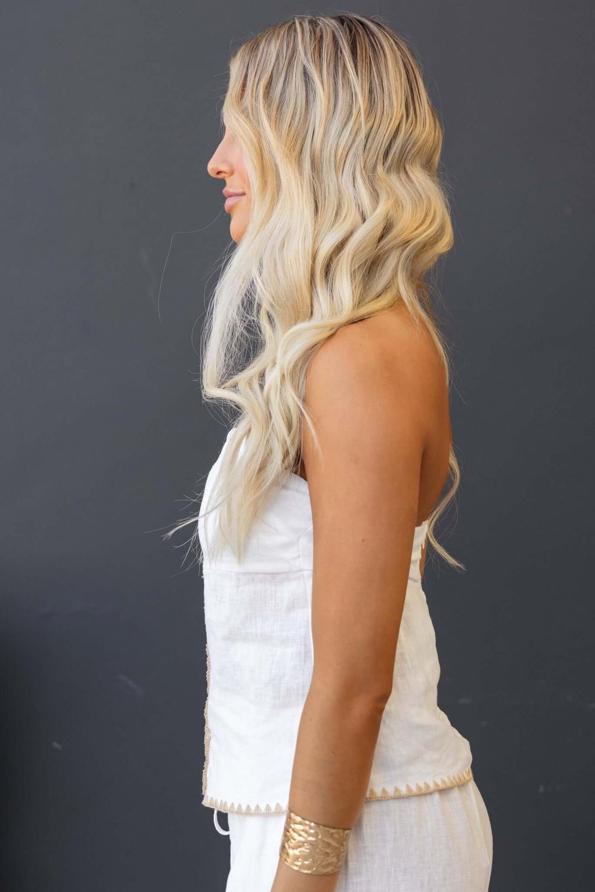 Side view of a woman in a strapless white linen top with a button-up front and styled wavy hair.