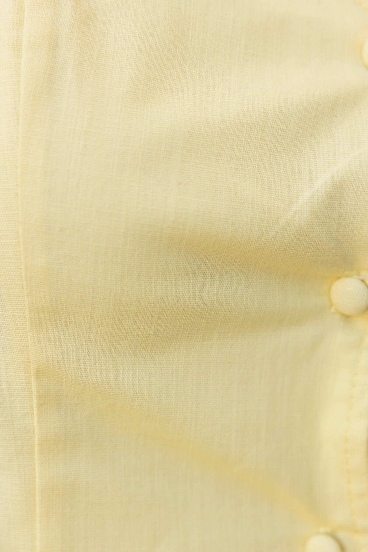 Close-up of smooth yellow fabric with button details, showcasing soft texture and color.