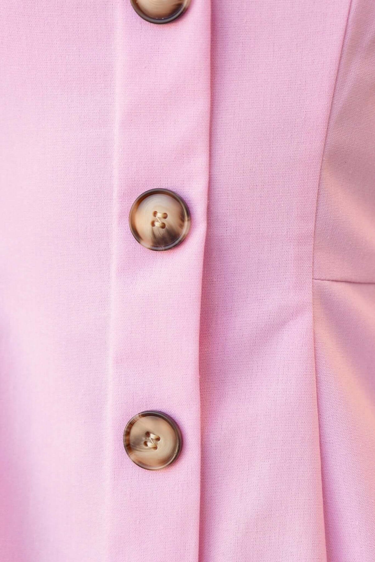 Close-up of Olean Dress showcasing faux buttons on a pink fabric, highlighting its stylish details.
