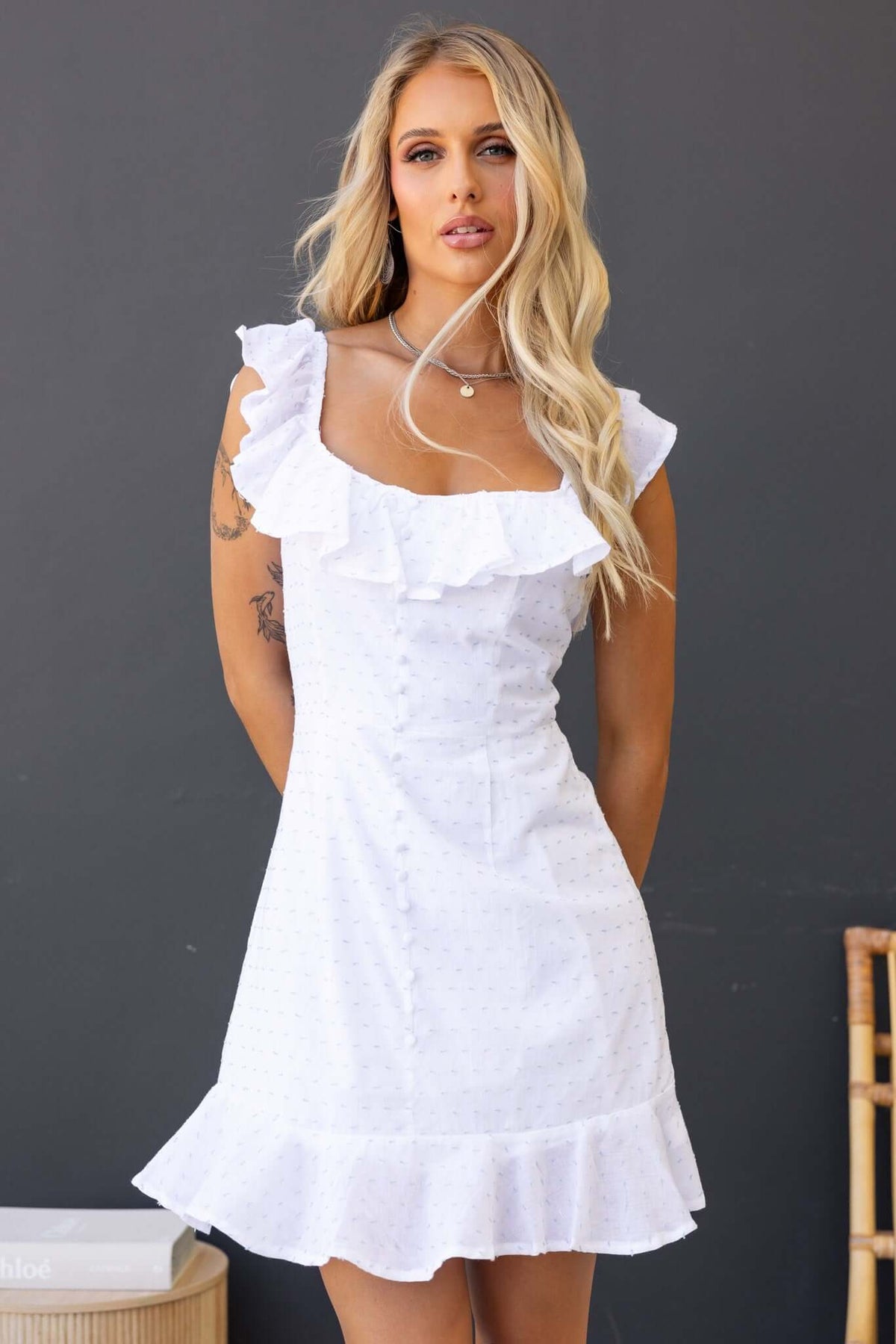 Off-shoulder white Harp Dress featuring ruffles and faux buttons, styled with a chic fit.
