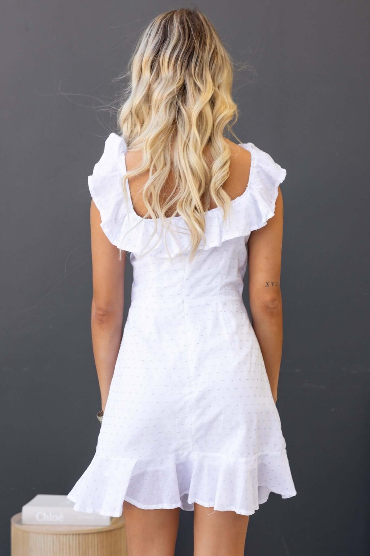 Back view of Harp Dress featuring off-shoulder design, ruffled neckline, and flared skirt in white cotton.