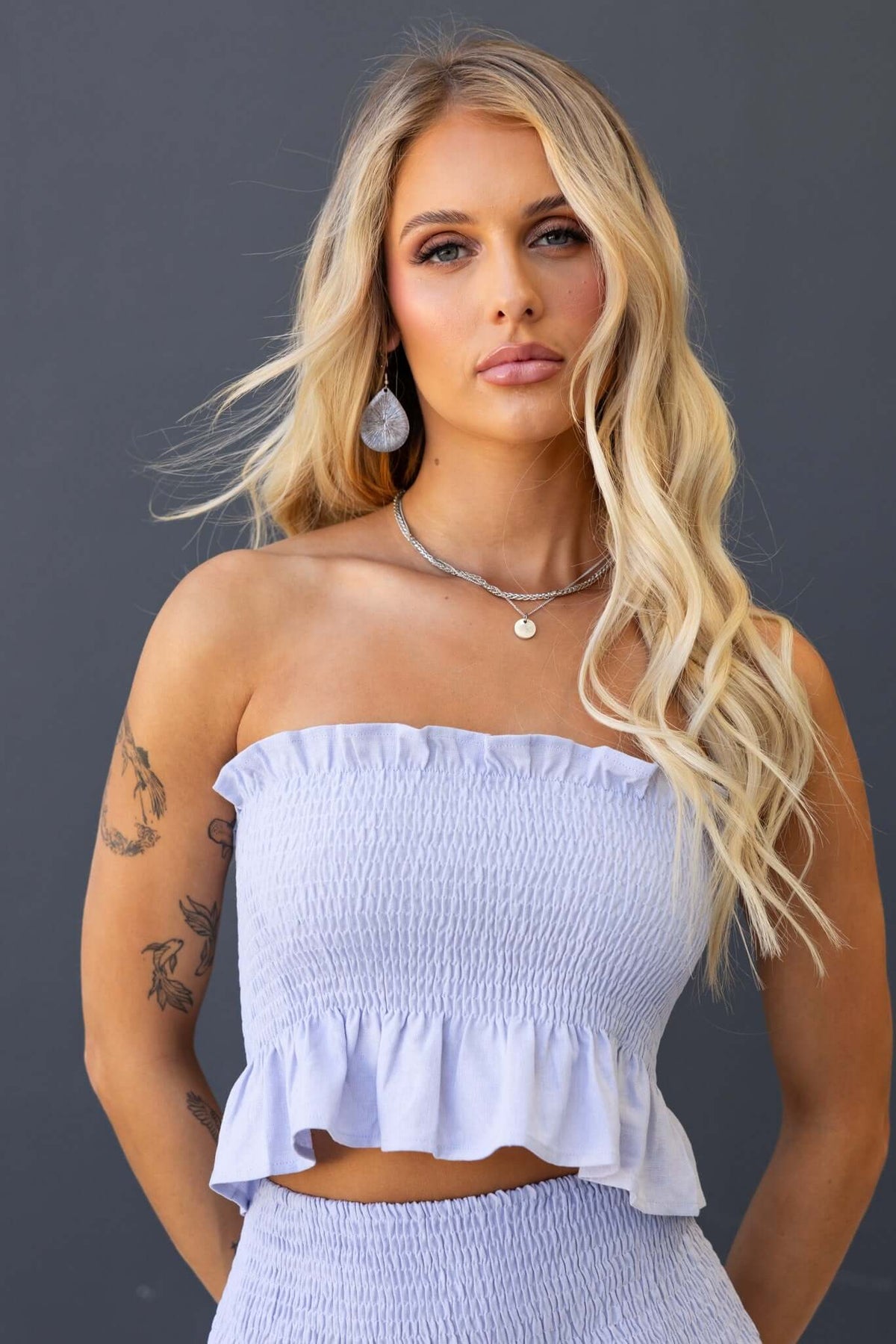 Nolan Top in lavender featuring an elastic bodice and ruffled hem, modeled by a woman with long hair and accessories.