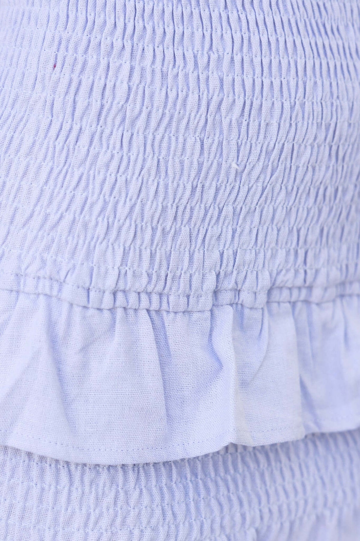 Close-up of the Nolan Skirt showing mid-high waist fit, elasticated texture, and layered ruffle hem in light blue.