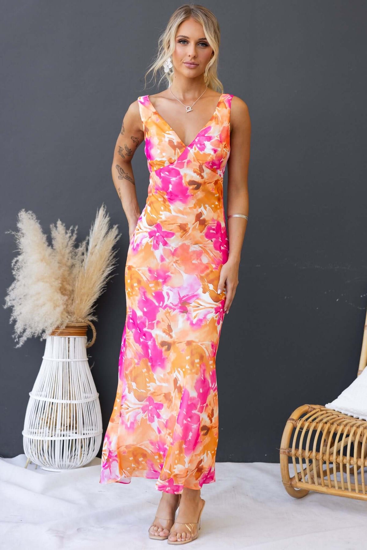 Model wearing Qilax Maxi Dress in vibrant orange and pink floral print, featuring a V-neckline and a flowing silhouette.