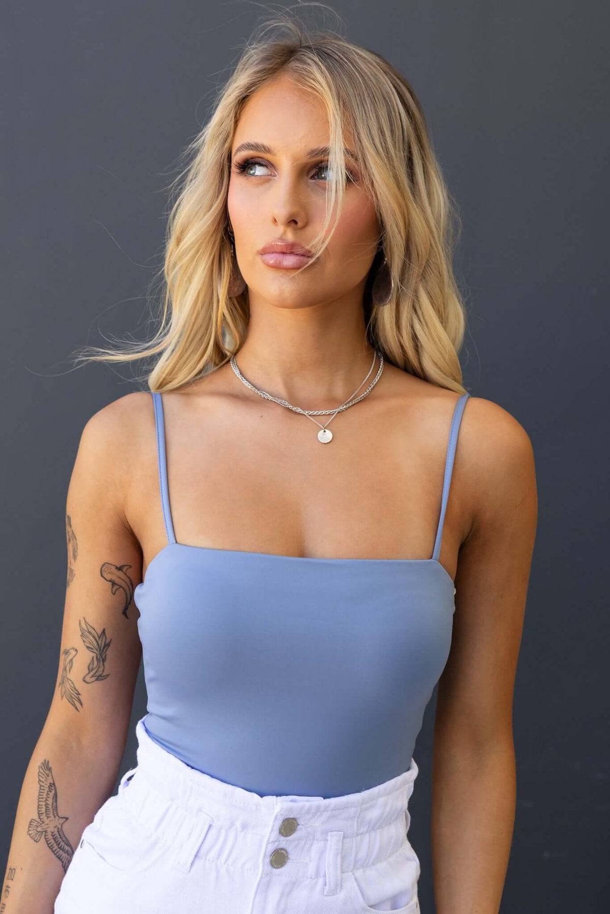 Model wearing the Paria Bodysuit in blue, featuring adjustable straps and a sleek design.