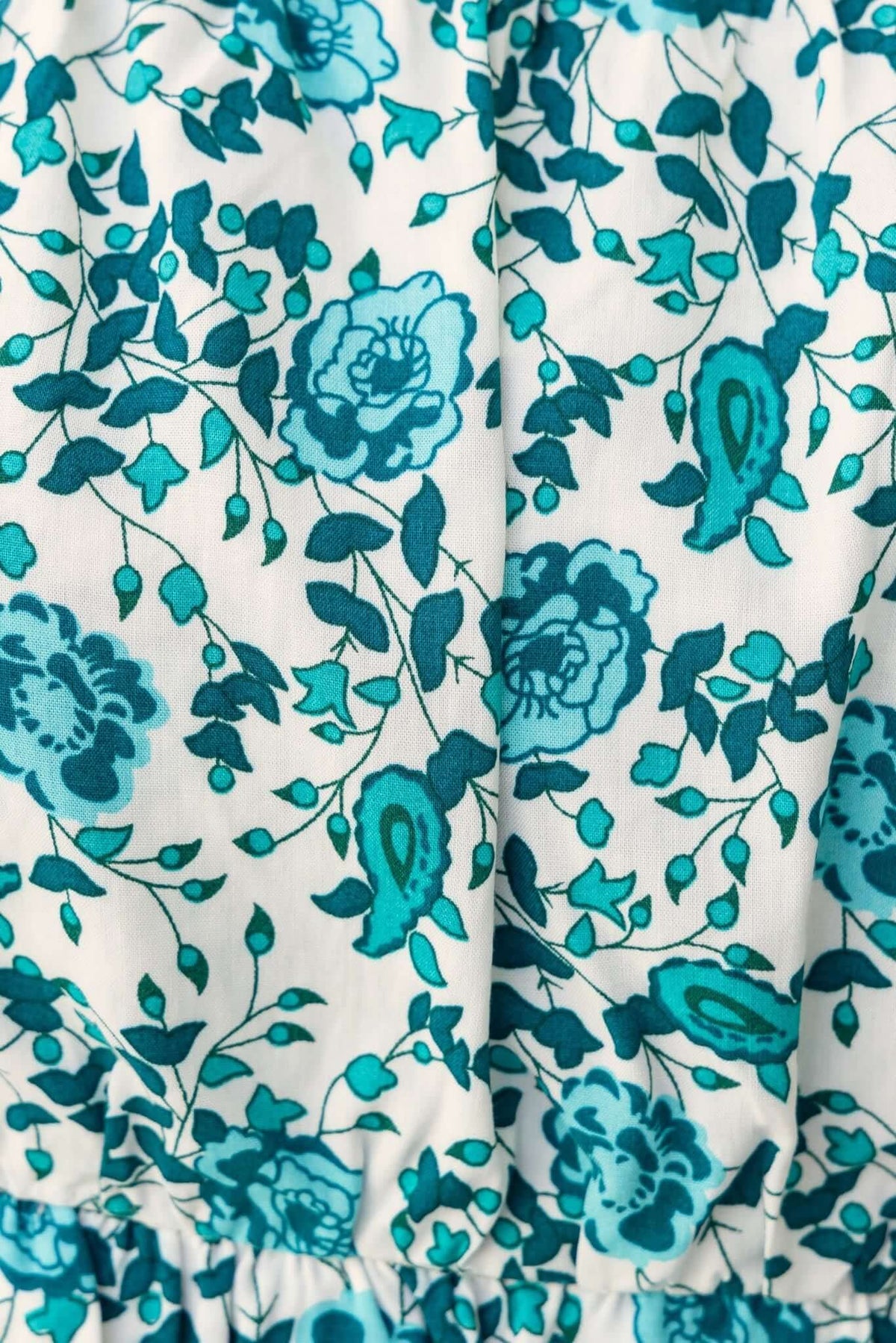 Close-up of Jana Top fabric with teal floral pattern, showcasing floral and paisley designs on a white background.