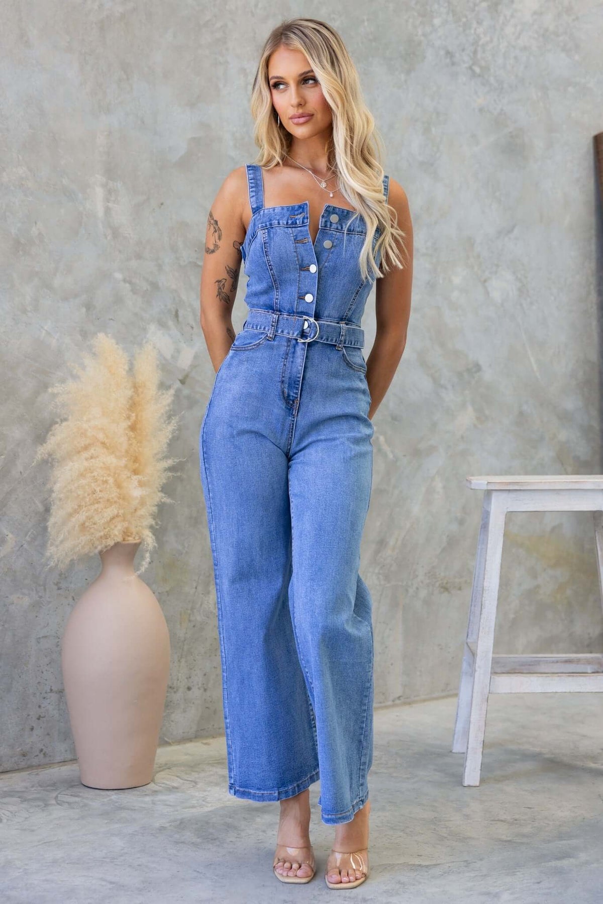 Josey Denim Jumpsuit featuring adjustable straps, button-up front, removable belt, and pockets.