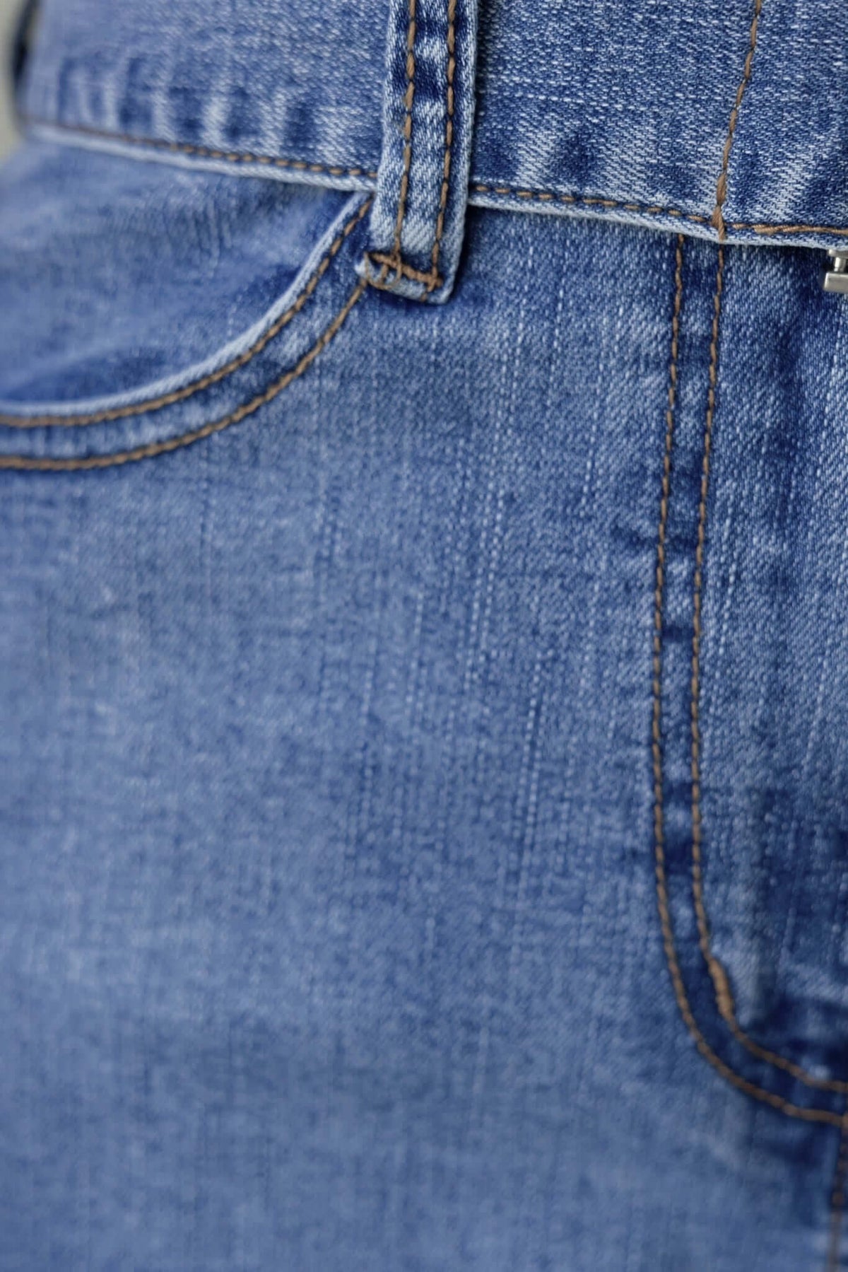 Close-up of the denim fabric of a jumpsuit, showing pocket and stitching details in a classic blue color.