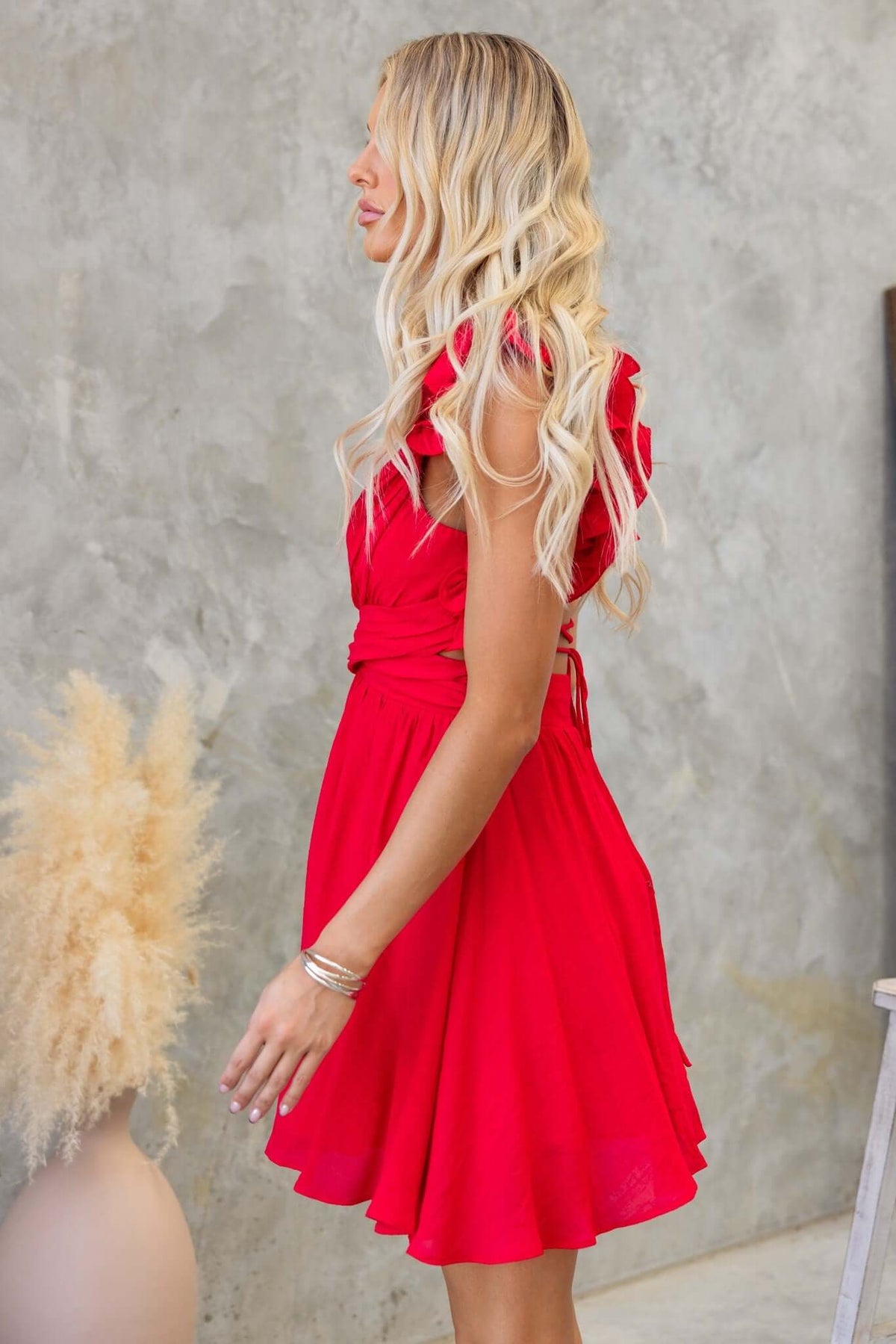 Model showing the Luciana Dress featuring ruffle straps and a cut-out waist in vibrant red chiffon.
