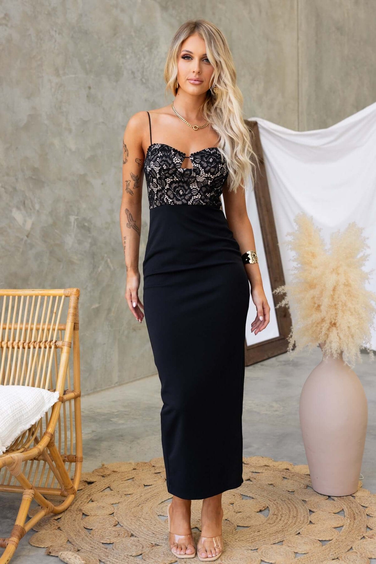 Model wearing a black Tempest Maxi Dress with adjustable straps and lace detailing, showcased in a stylish interior setting.