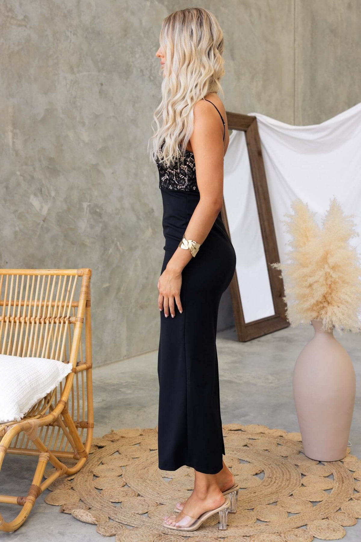 Side view of a woman in a black Tempest Maxi Dress with adjustable straps and a split at the back.