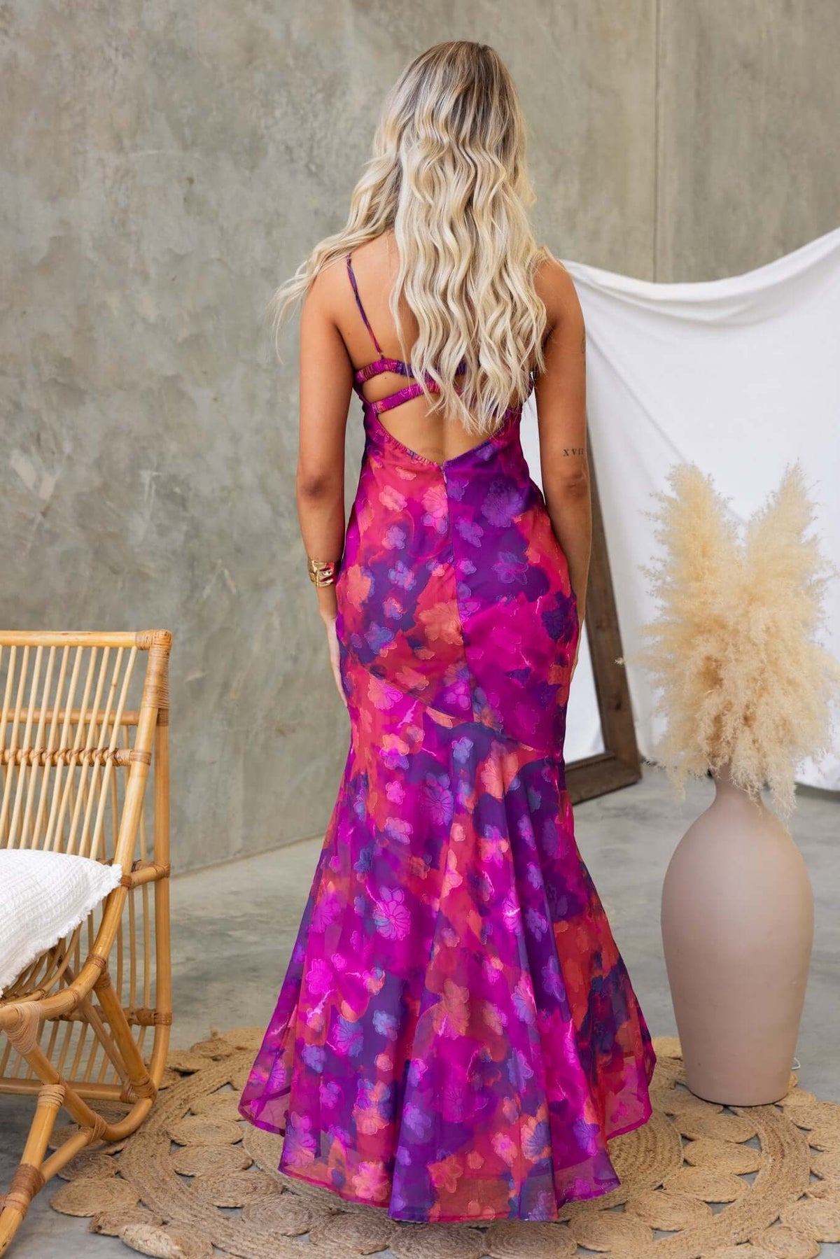 Back view of the Fontana Maxi Dress with adjustable straps and vibrant purple floral pattern, styled in a modern indoor setting.