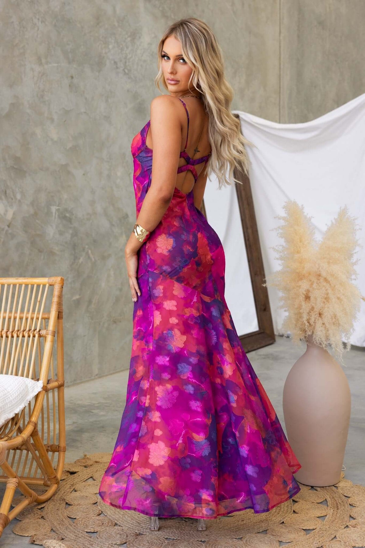 Back view of a woman in a vibrant pink and purple Fontana maxi dress with adjustable straps and a high-low hem.