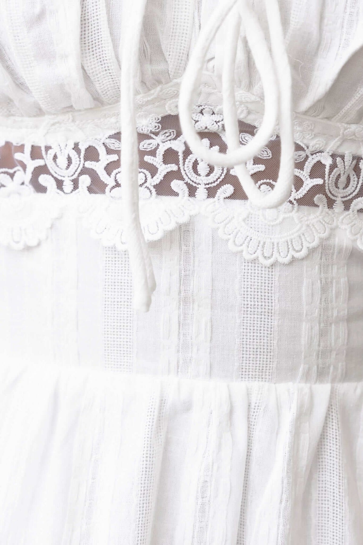 Close-up of Haizel Dress featuring a sheer panel and delicate lace detailing at the waist in white cotton fabric.