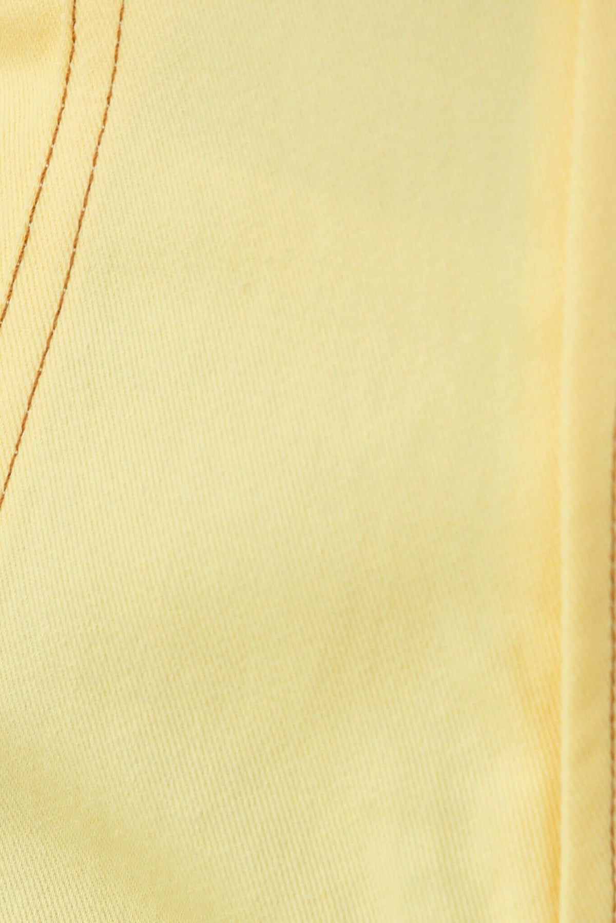 Close-up of light yellow fabric with fine stitching details, showcasing texture and color.