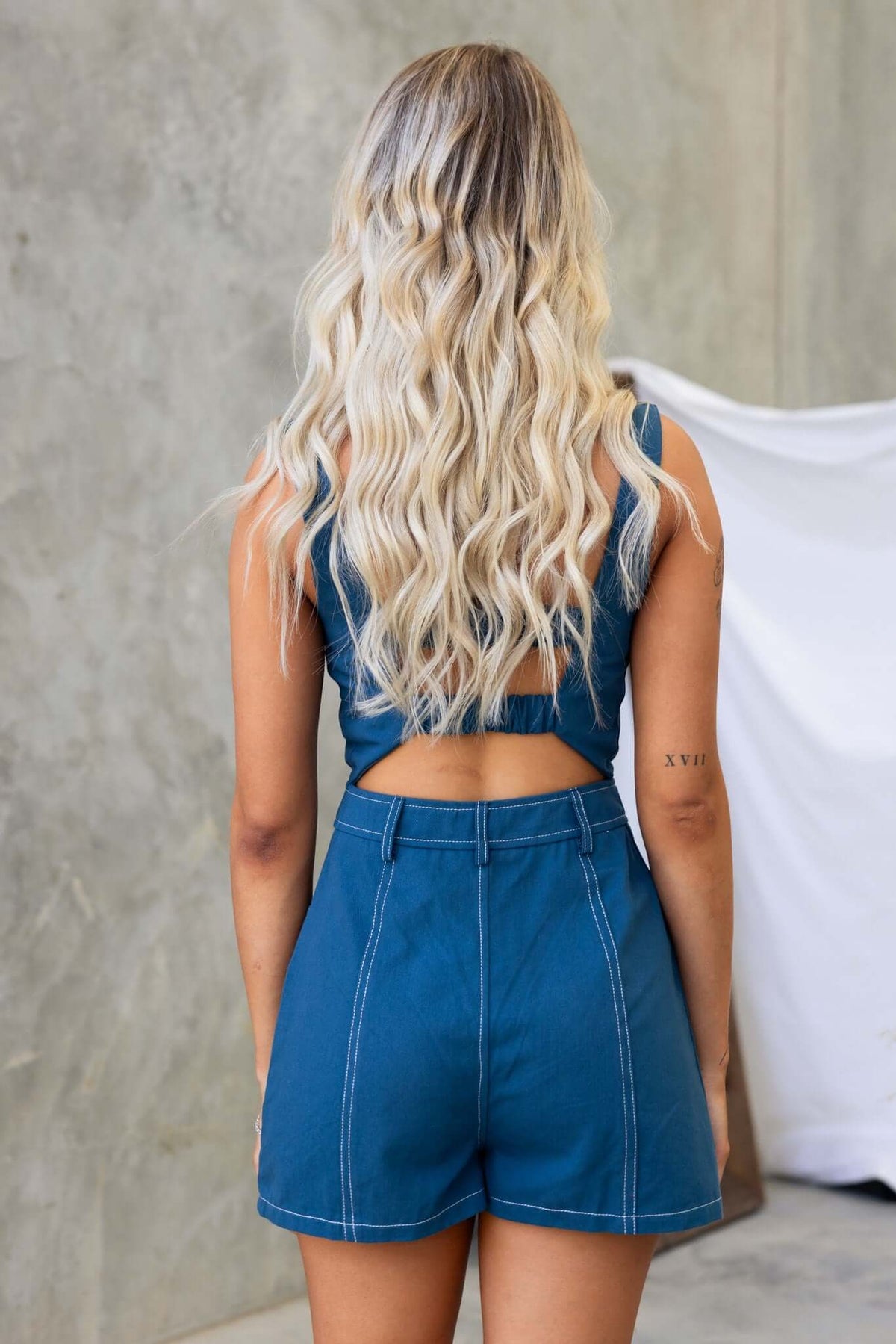Back view of a model wearing a Salone Denim Playsuit with a cut-out detail and casual beachy waves hairstyle.