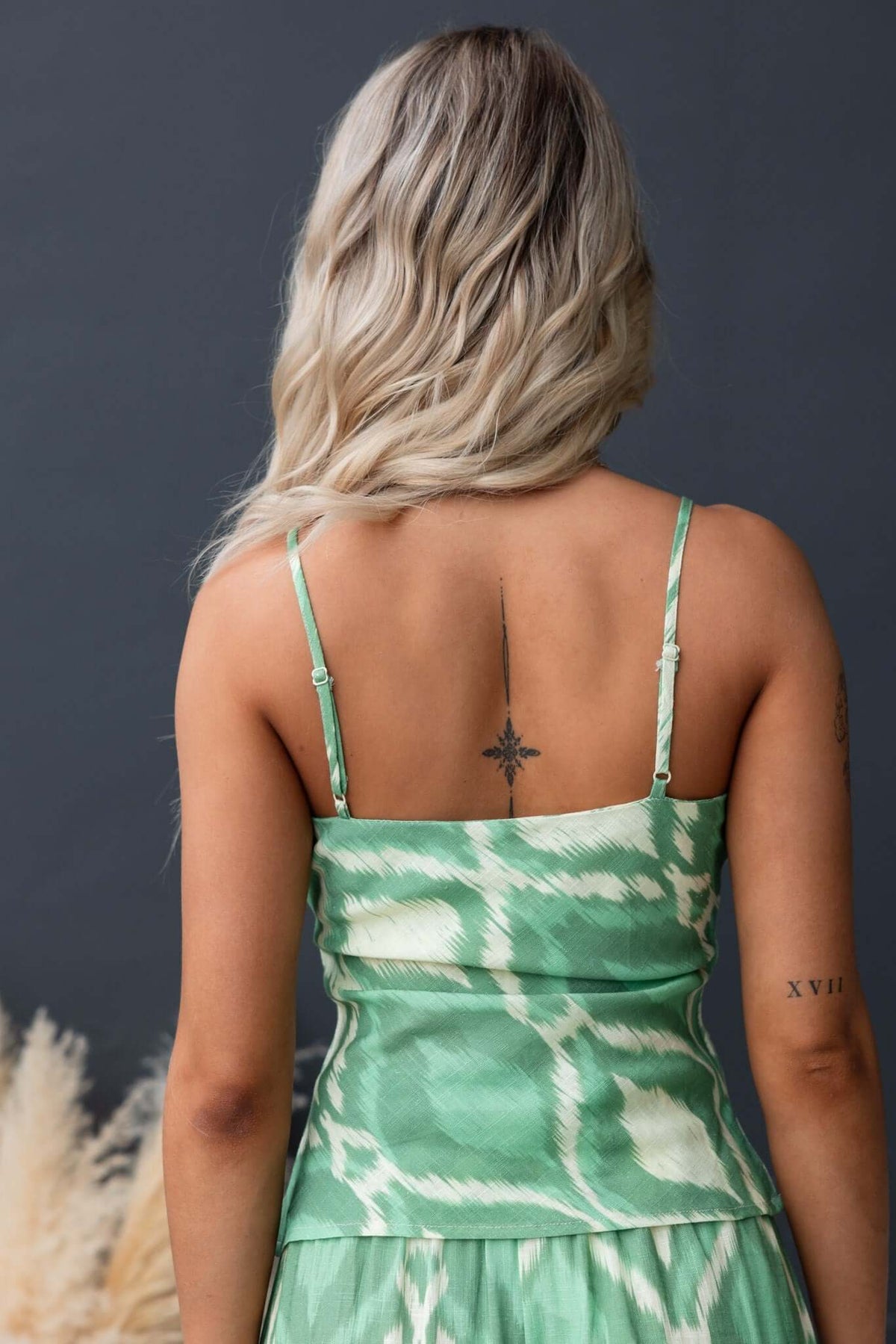 Back view of a woman in a green Mason Top with adjustable straps, showcasing its stylish design and fabric texture.