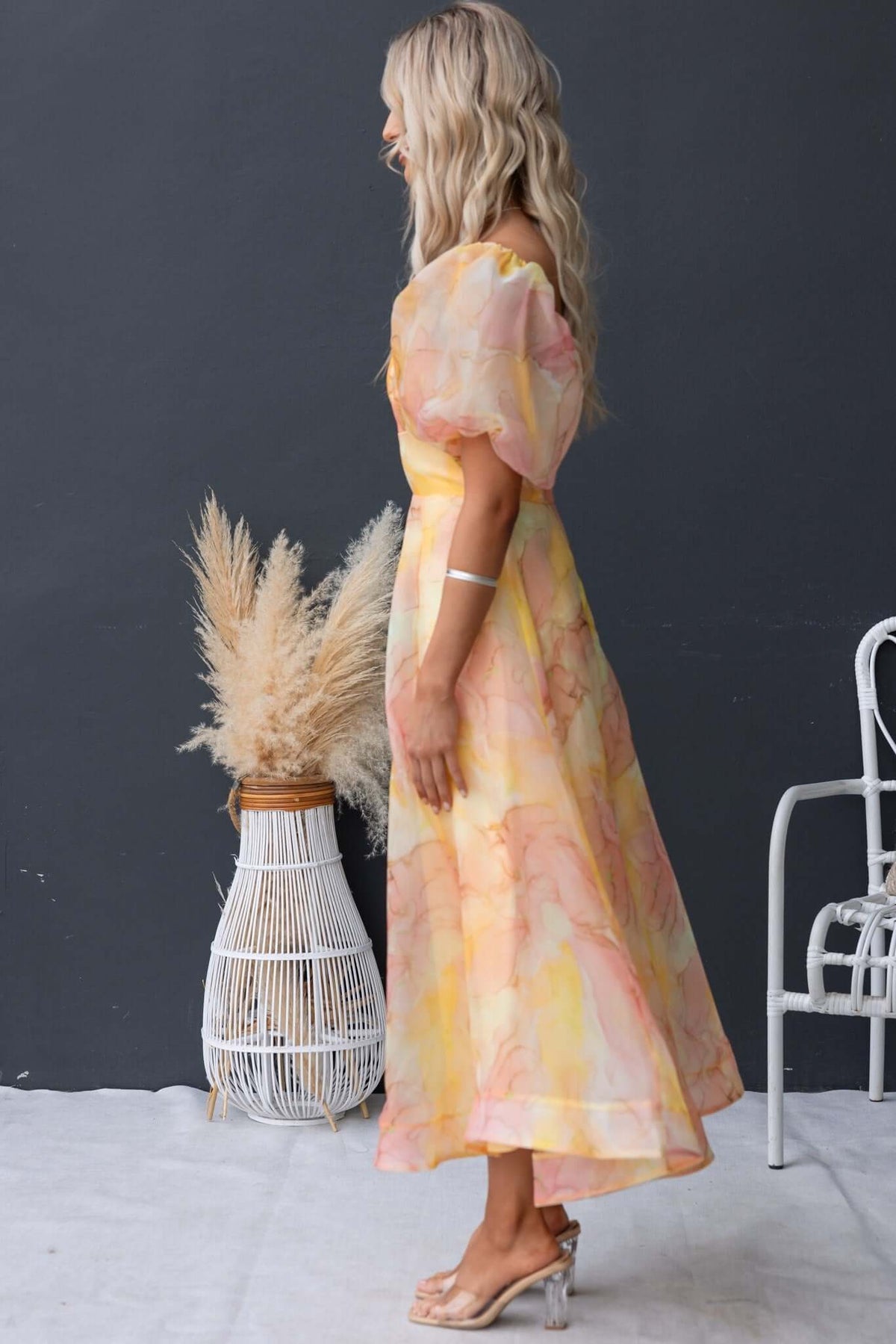 Model wearing a Nerine Maxi Dress in pastel colors with puff sleeves, showcasing a flowy design against a minimalist backdrop.