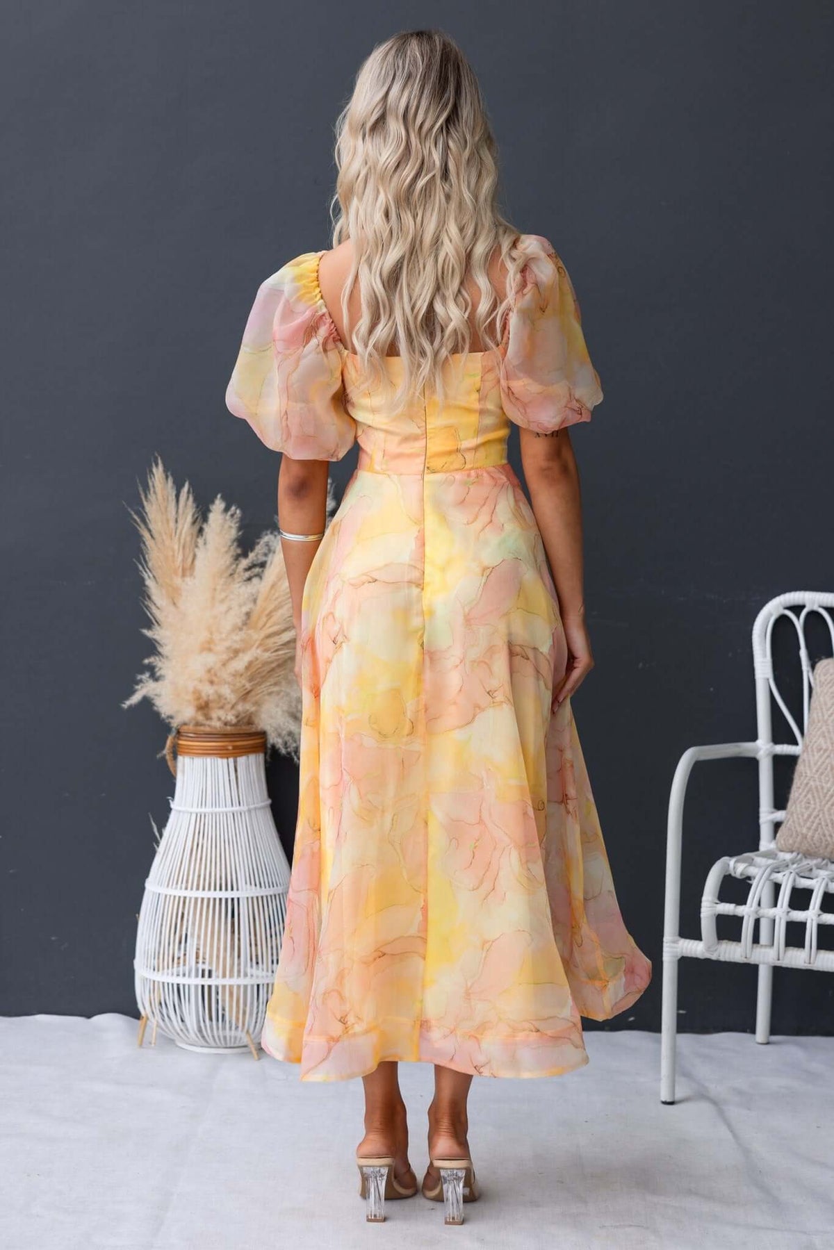Back view of a model wearing the Nerine Maxi Dress with puff sleeves and floral pattern, styled against a modern backdrop.