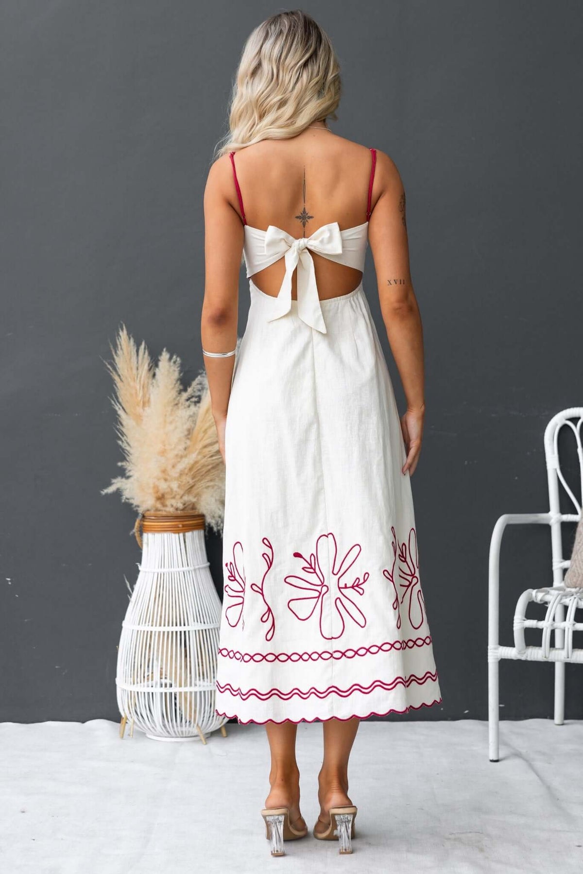 Back view of a woman in a Homestead Midi Dress with a tie detail, featuring floral embroidery and adjustable straps.