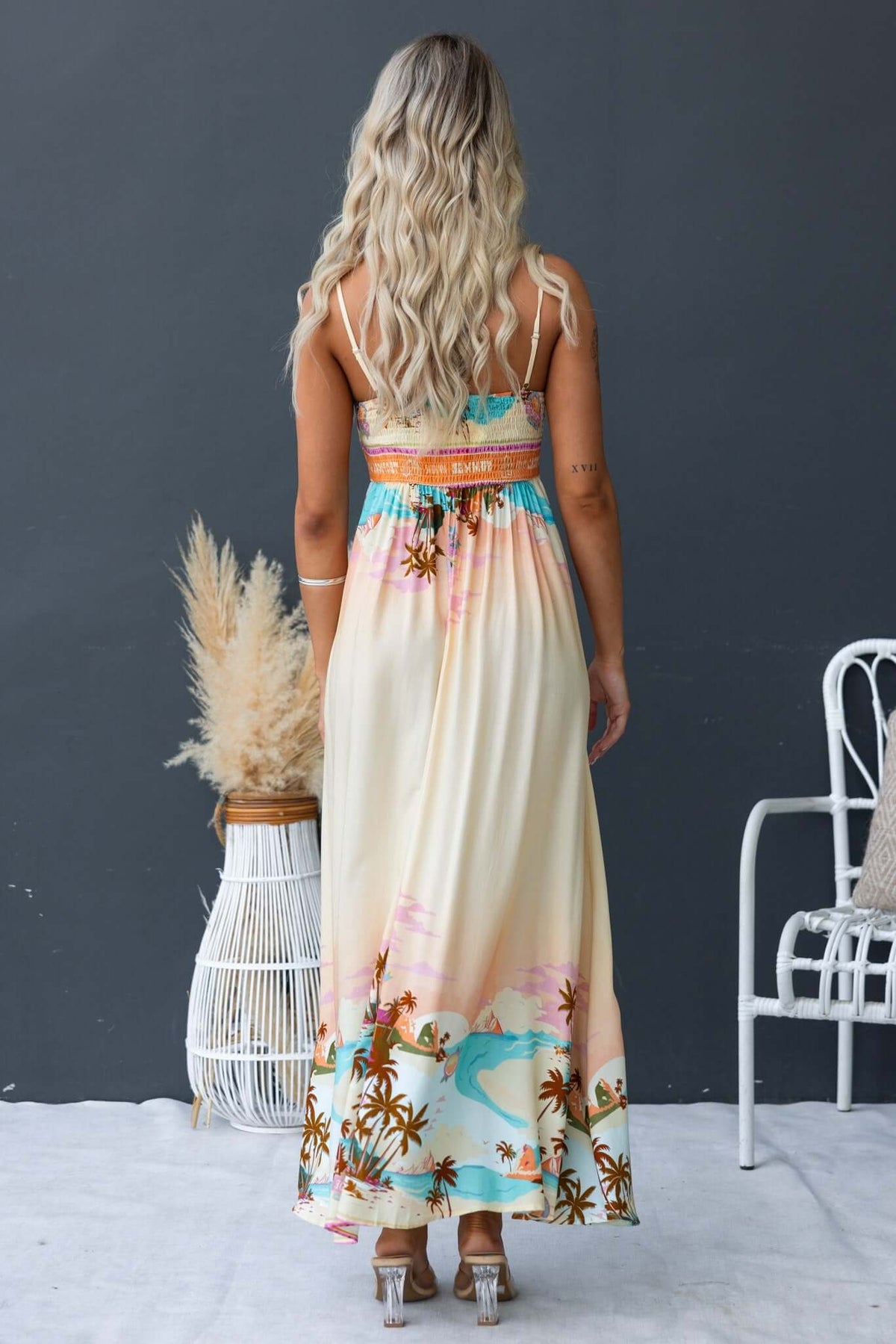 Back view of a woman in a Salilah Maxi Dress with adjustable straps and tropical print, featuring shirred panel and pockets.