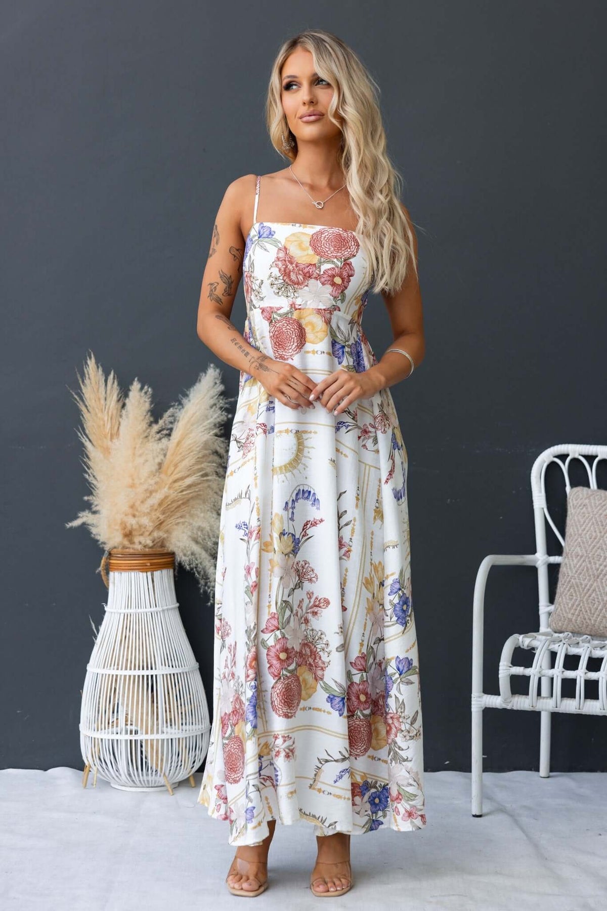 Model wearing the Salilah Maxi Dress with floral print, thin straps, shirred back, and pockets, styled in a modern setting.