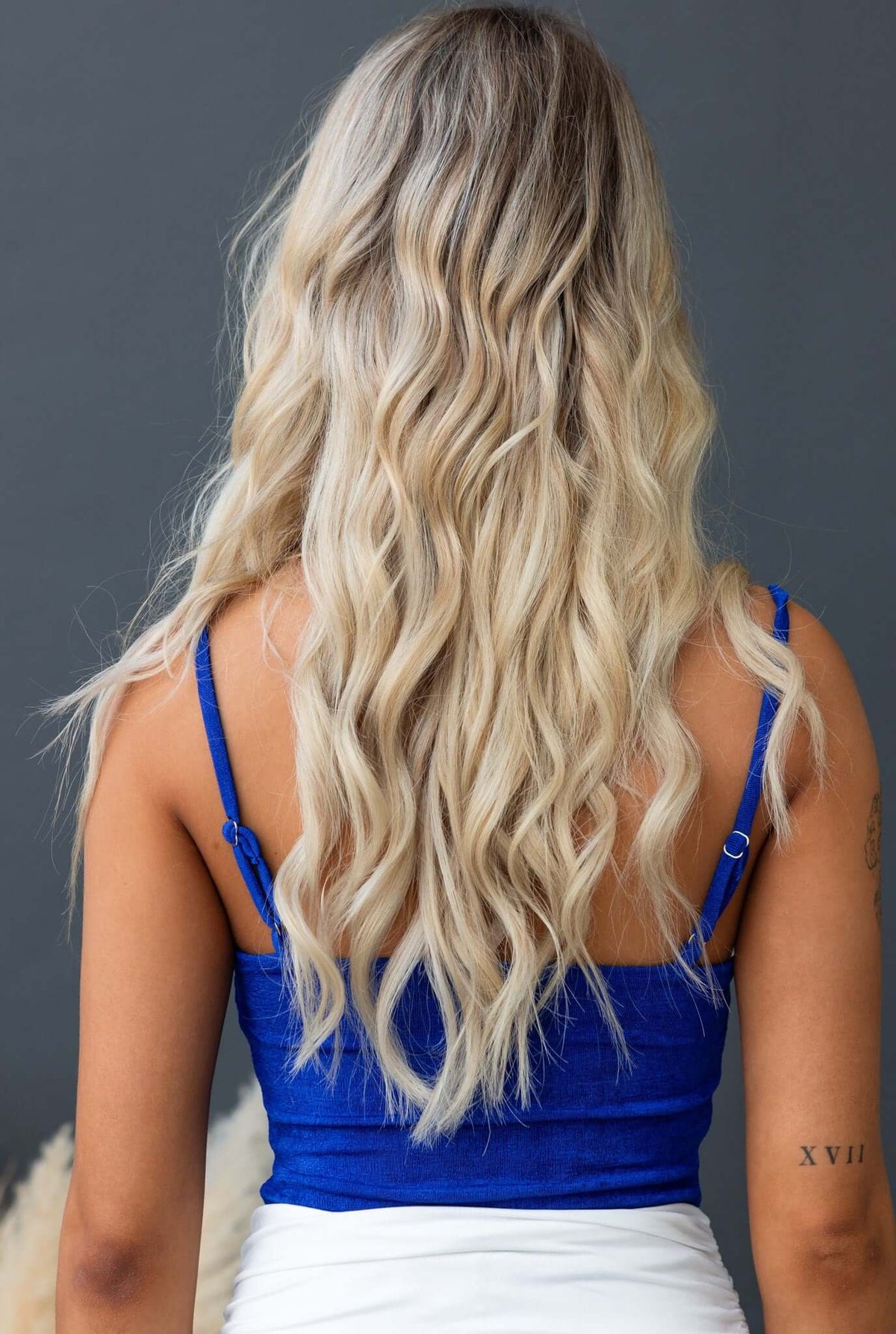 Back view of a woman in a blue Brea bodysuit with adjustable straps, showcasing her long, wavy blonde hair.