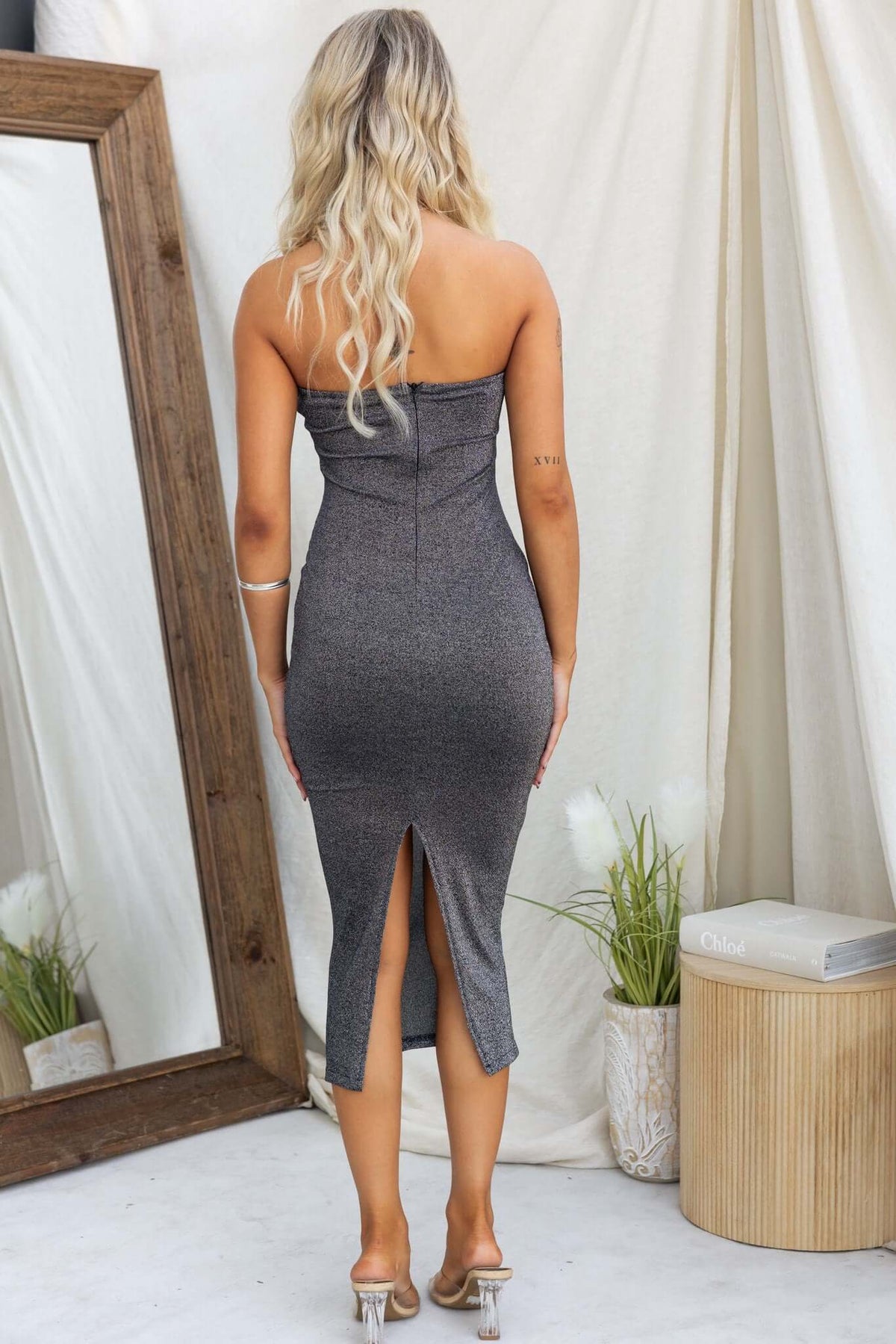 Back view of a black strapless Ellodia midi dress with a split, showcasing its metallic fabric and fitted design.