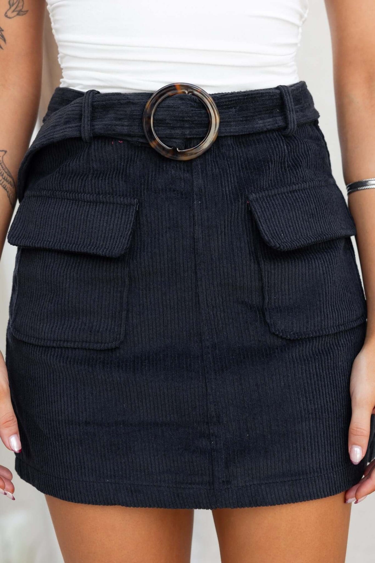 Black corduroy Pierre skirt with removable belt, pockets, and mid-high waist fit.
